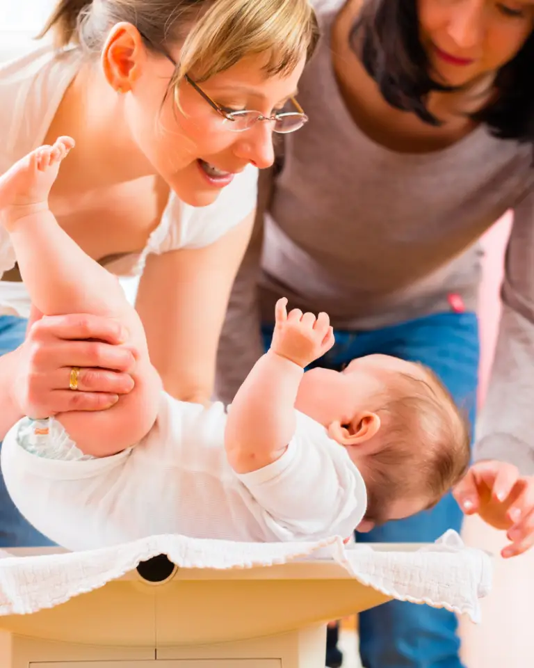 Hebamme betreut lächelnd ein Baby auf dem Wickeltisch, daneben die Mutter