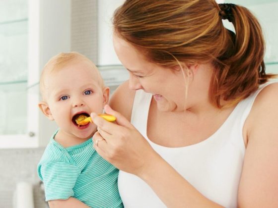 Mama füttert ihr Baby im Arm mit Brei