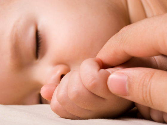Baby besser schlafen lassen – schlafendes Baby hält beruhigend den Finger eines Elternteils